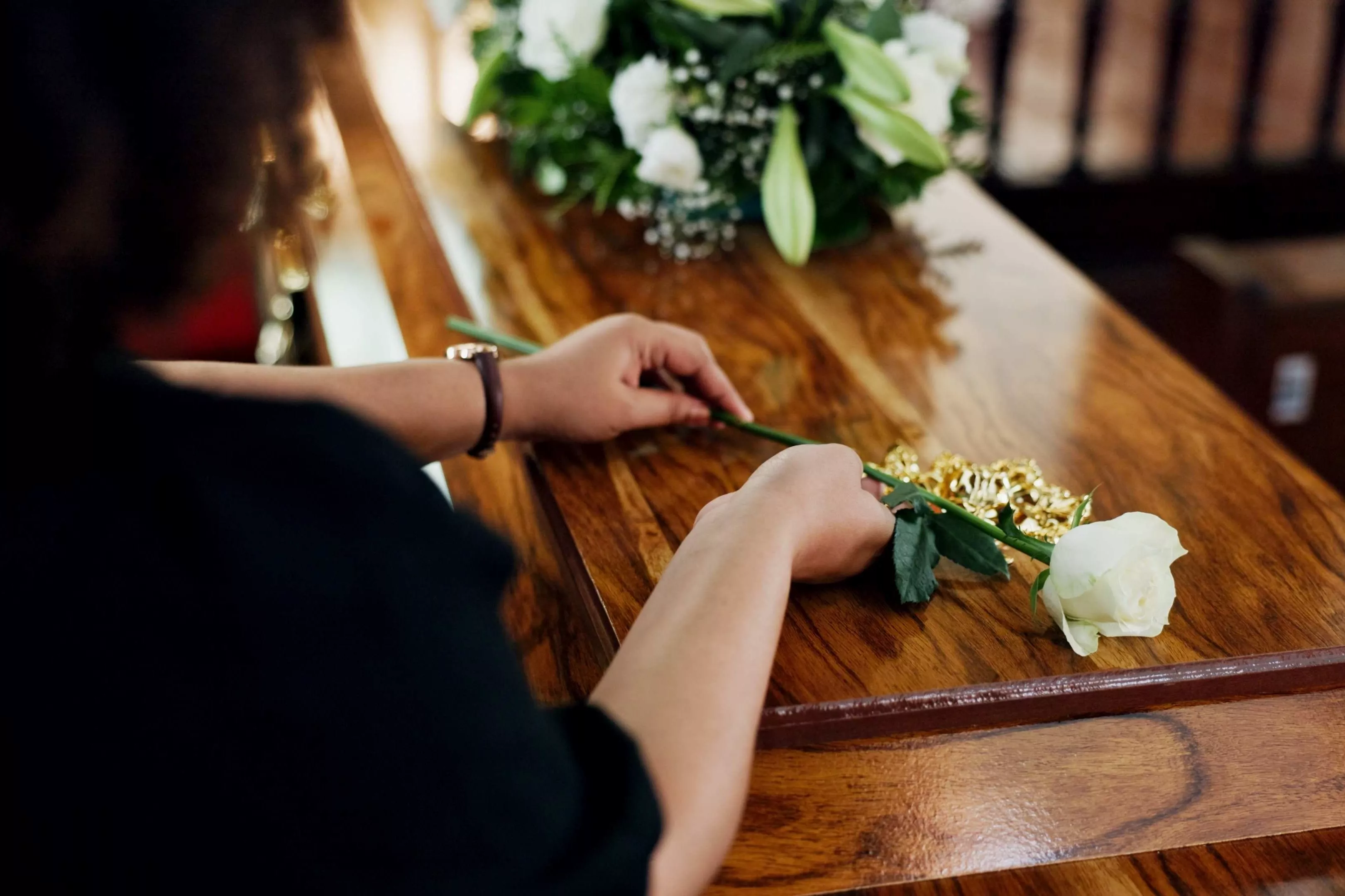 Eine Frau legt eine weiße Rose auf einen Sarg